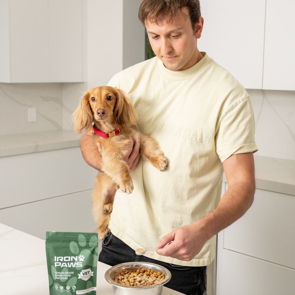Dog dad holding his dachshund while scooping Iron Paws into its bowl